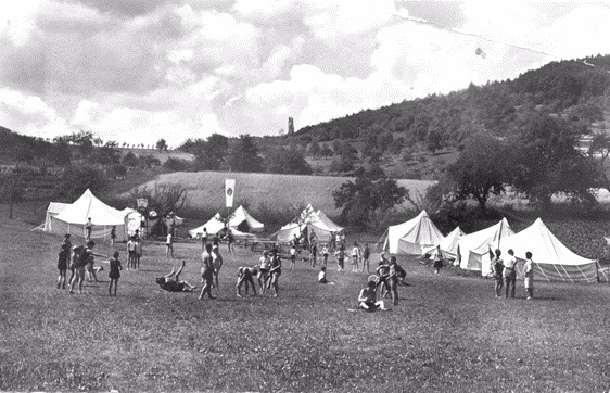 Weite Wiese mit mehreren Zelten und spielenden Kindern bei einer Veranstaltung im ländlichen Tal.