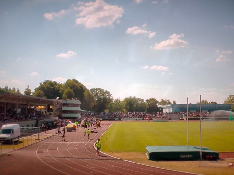 Leichtathletikstadion mit Laufbahn, Tribünen und Sprunggrube im Gegenlicht; Blick auf Sportgeschehen und Wettkampfbereich.