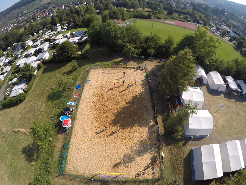 Luftaufnahme eines Sportplatzes mit mehreren Fußballfeldern, Spielerkreiskreisen und Zelten am Rand; zeigt eine Veranstaltung.