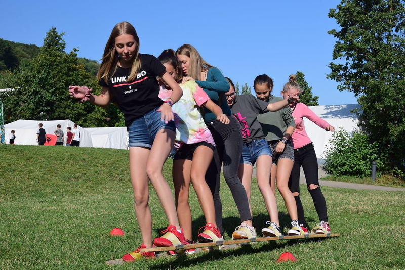 Gruppe Kinder balanciert auf einer Holzbank im Freien und trainiert gemeinsam Geschicklichkeit und Gleichgewicht.