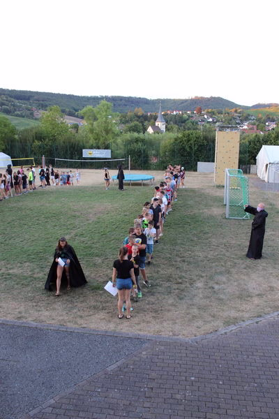 Kinder gehen als Gruppe über den Rasen zu einem Sport- und Spielfeld bei einer Outdoor-Veranstaltung, um an Aktivitäten teilzunehmen.