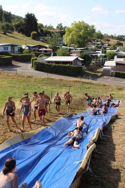 Camp-Sporttag: Jugendliche liegen auf einer blauen Plane im Freien am Rand eines Wegs, daneben Sport- und Spielgeräte, Aussicht über das Gelände.