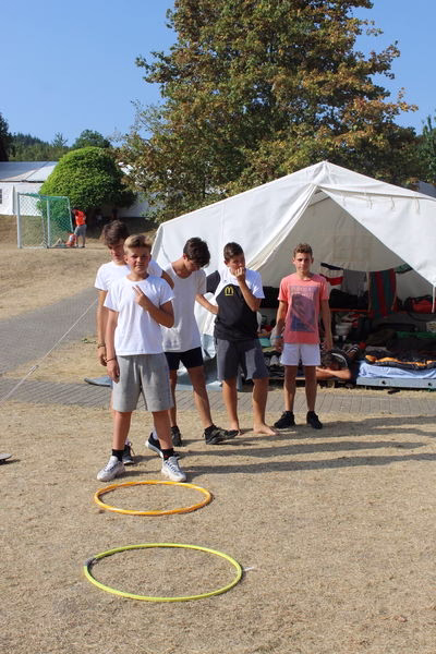 Kinder spielen im Freien mit Hula-Hoop-Reifen vor einem Zelt; die Reifen zeigen die Parcours-Übung während einer Sportaktion.