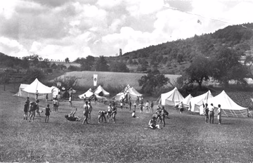 Zeltplatz in einer Berglandschaft mit Menschen, die ein Gelände als Veranstaltungsgelände vorbereiten und begehen.